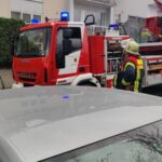Feuerwehrfahrzeug mit ausgefahrener Drehleiter vor Wohnhaus, Feuerwehrmann in Schutzkleidung