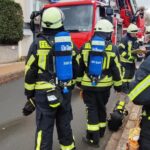 Feuerwehrleute mit Atemschutzgeräten vor Löschfahrzeug mit Drehleiter bei Wohnhauseinsatz